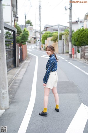 A woman in a blue shirt and white shorts walking down a street.