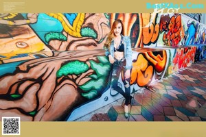 A woman sitting on the ground in front of a graffiti covered wall.