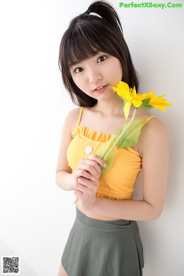 A woman in a yellow top holding a yellow flower.