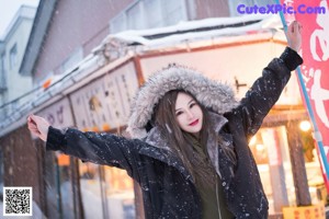 A woman in a green bodysuit is posing in the snow.