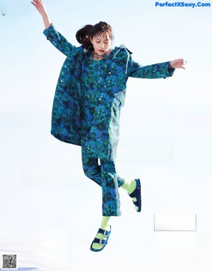 A woman in a colorful jacket and blue pants is jumping in the air.