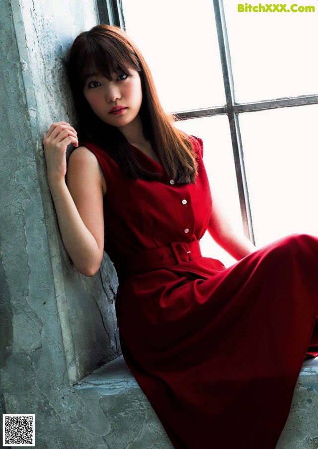 A woman in a red dress leaning against a window.