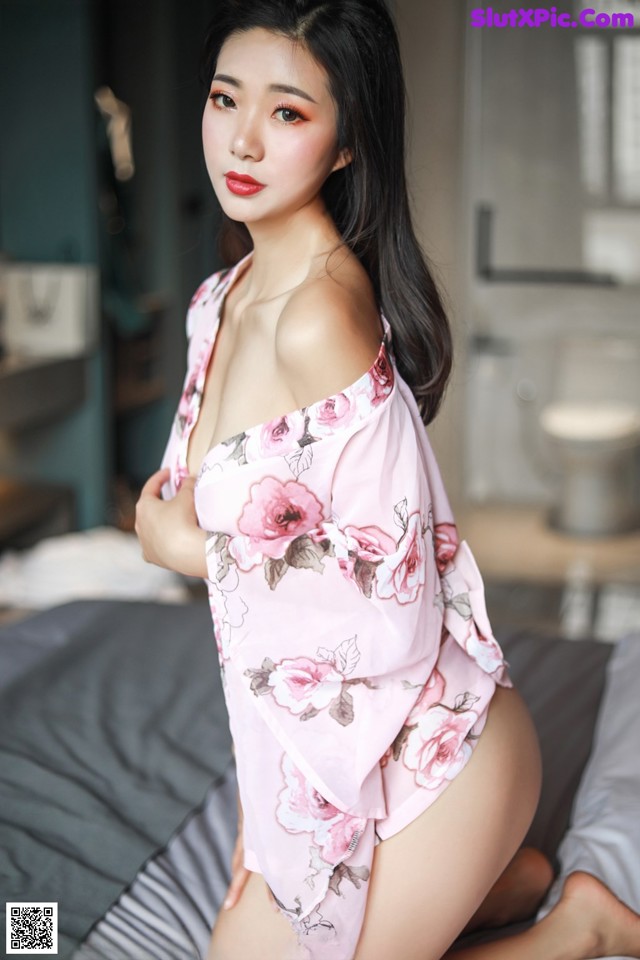 A woman in a pink robe sitting on a bed.