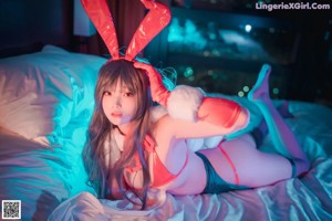 A woman in a red bunny costume sitting on a bed.