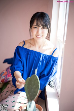 A woman in a blue top standing by a window.