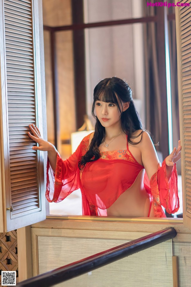 A woman in a red lingerie leaning against a window.
