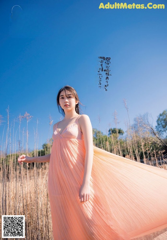 A woman in a long pink dress standing in a field.