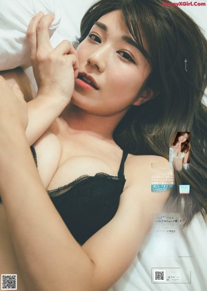 A woman in a black lingerie sitting on a bed.