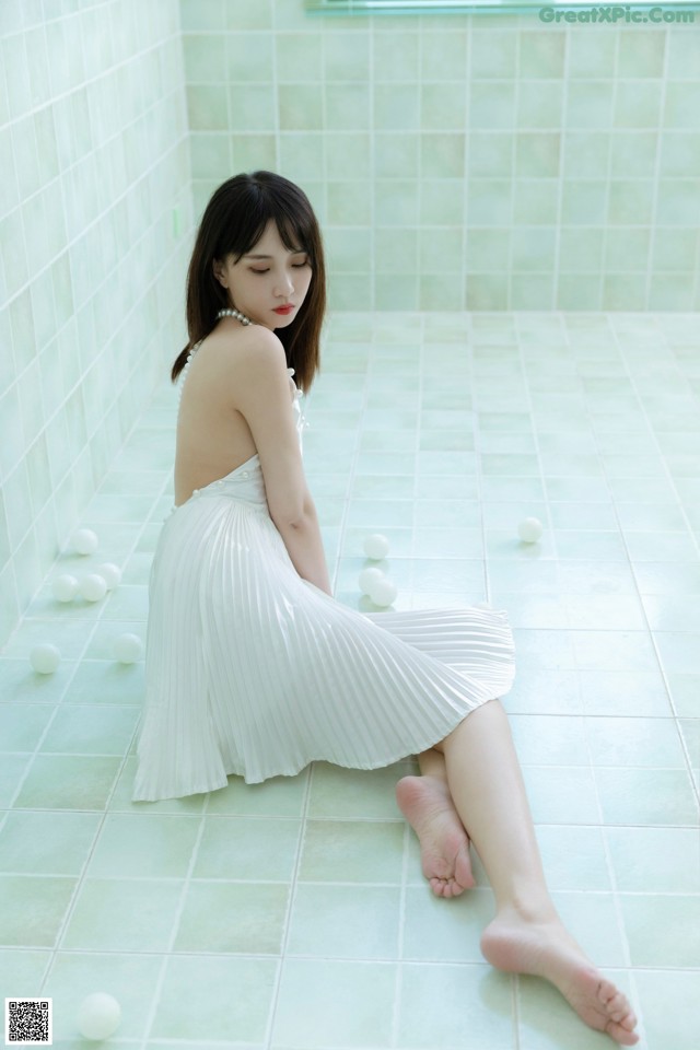 A woman in a white dress sitting on the floor.