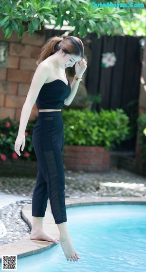 A woman standing next to a swimming pool in a black top and pants.