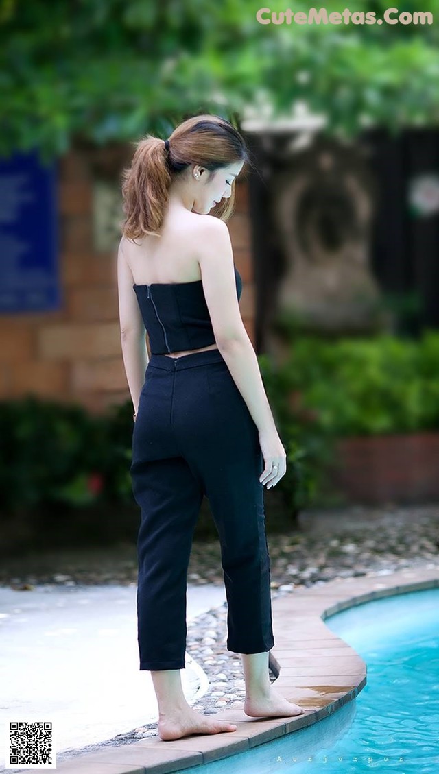 A woman standing next to a swimming pool in a black top and pants.
