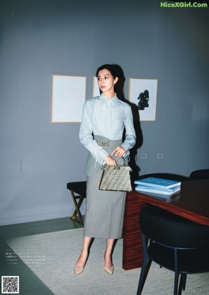 A woman standing in front of a desk holding a blue bag.