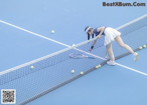 A woman sitting on a tennis court next to a net.