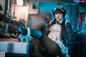 A woman in a maid outfit sitting on a chair.