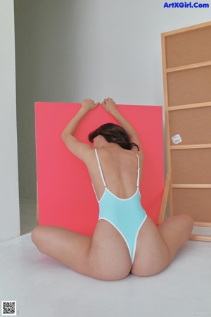 A woman in a blue bodysuit leaning against a white wall.