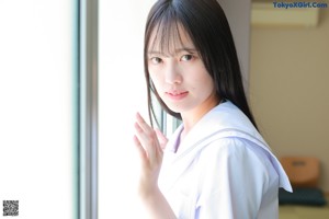 A woman in a school uniform standing by a window.