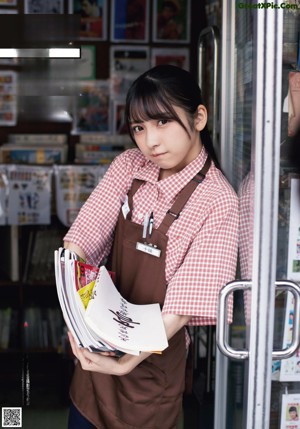 A woman sitting on a stool in front of a book shelf.