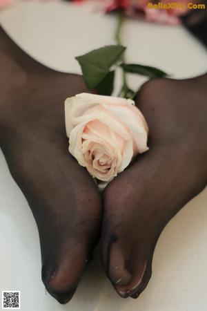 A woman in black stockings holding a pink rose on a table.