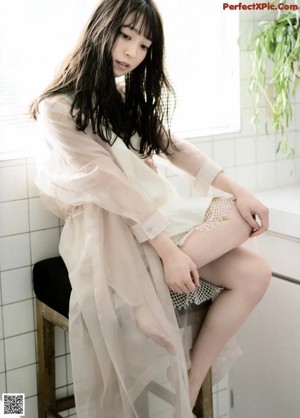 A woman in a white dress sitting on a bed.
