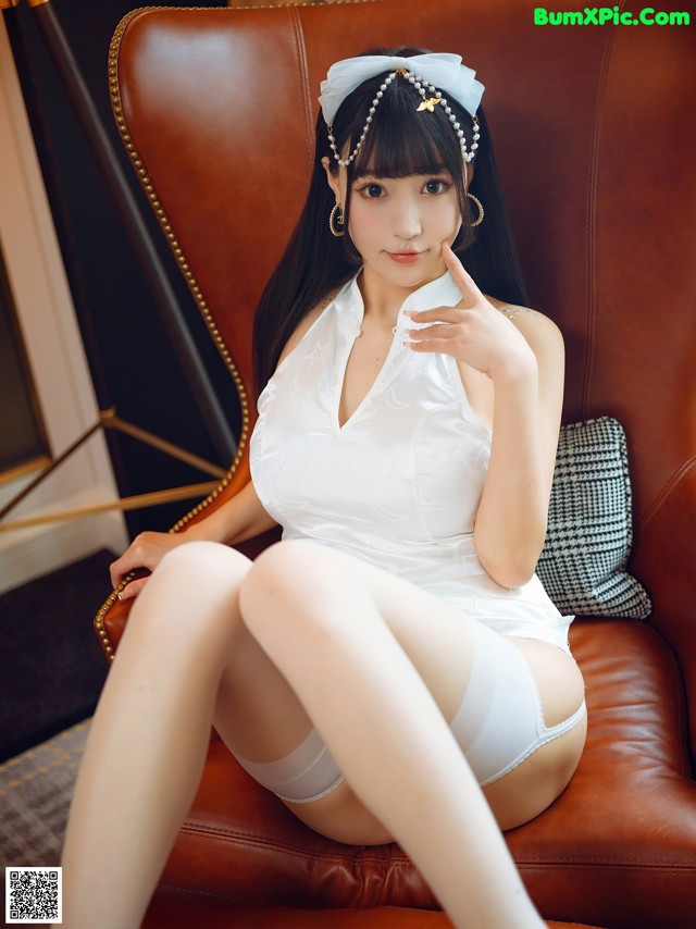 A woman in a white dress sitting on a brown chair.